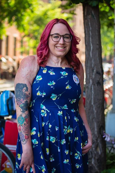 a person with red hair and glasses standing next to a tree