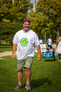 A man with a purple bandana on his head smiling and wearing a NEDA t-shirt.