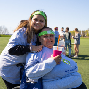 Two women, wearing Green bandanas and NEDA t-shirts smiling at the camera. One is seated in a wheelchair.