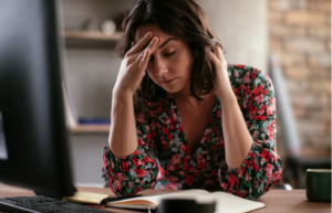 Woman sitting at desk with hand on head- representing the physical effects of an eating disorder